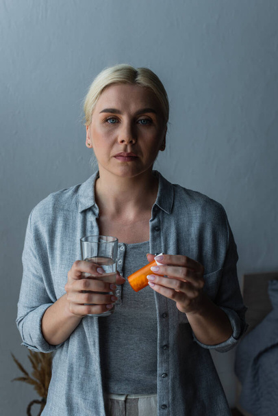 blonde woman with menopause holding glass of water and bottle with medication - Photo, Image