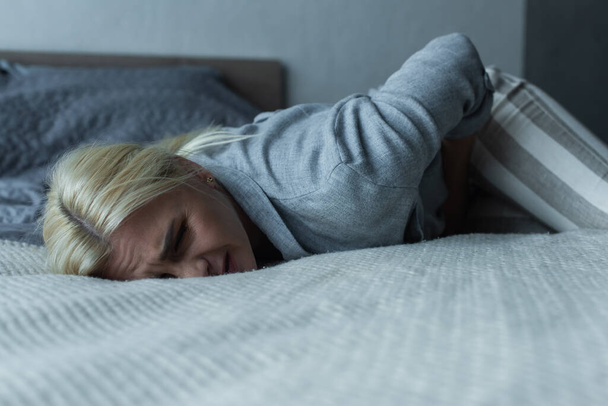 stressed woman lying on bed while feeling pain in stomach during menopause  - Photo, image