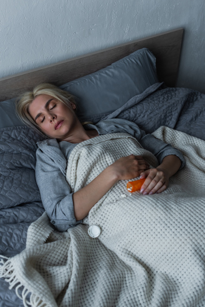 high angle view of depressed blonde woman with menopause sleeping near pills in bed - Fotografie, Obrázek