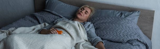 depressed blonde woman with menopause sleeping near pills in bed, banner - Foto, imagen