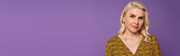 happy and blonde woman in blouse looking at camera isolated on purple, banner - Fotoğraf, Görsel