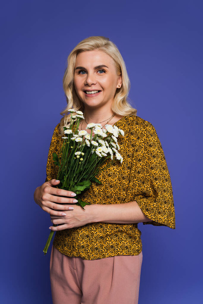 happy woman in blouse holding bouquet of white flowers with green leaves isolated on violet - Fotografie, Obrázek