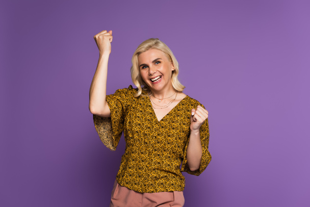 happy blonde woman in blouse having menopause and rejoicing on purple  - Foto, Imagen