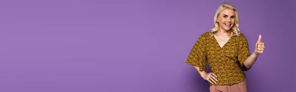 joyful blonde woman with menopause smiling and showing thumb up on purple, banner - Valokuva, kuva