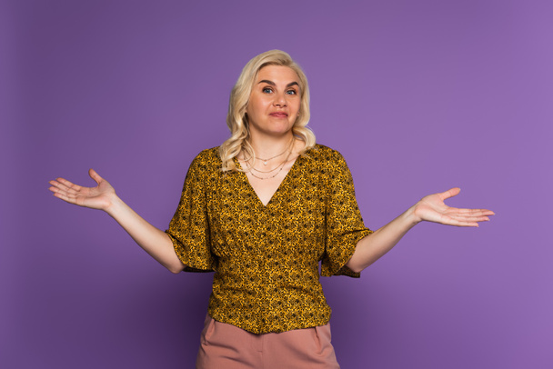 confused blonde woman with menopause showing shrug gesture on purple - Foto, Bild