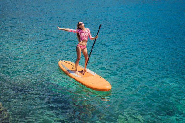 Young women Having Fun Stand Up Paddling in blue water sea in Montenegro. SUP. girl Training on Paddle Board near the rocks. - Foto, imagen