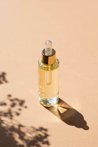 Transparent bottle with dropper pipette with serum or essential oil with beautiful flowers shadows. Beige background with daylight. Beauty concept for face and body care - Foto, imagen