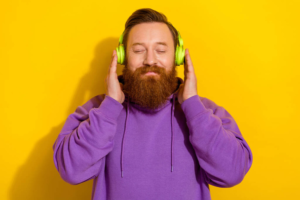 Photo of cute charming guy dressed purple sweater arms headphones enjoying music isolated yellow color background. - Φωτογραφία, εικόνα