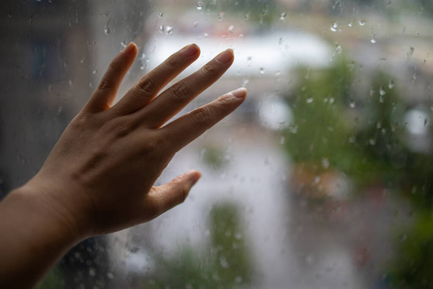 Regenwetter. Regen auf Glas. Regentropfen auf Fensterglas. Selektiver Fokus. Fenster mit der Hand berühren. - Foto, Bild