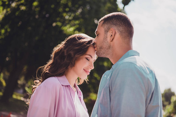 Photo of dreamy charming boyfriend girlfriend wear casual outfits kissing forehead enjoying sunny weather outdoors garden. - Foto, afbeelding
