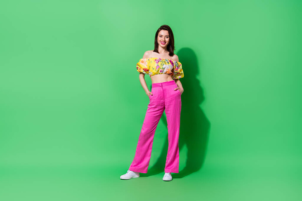 Full size portrait of pretty cheerful young person put arms pockets posing isolated on green color background. - Foto, Imagen
