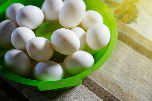 разнообразные белые яйца, сгруппированные в зеленой чаше на столе и мягкой стороне освещения - Фото, изображение
