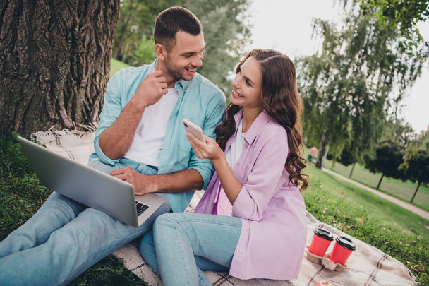 Photo of pretty sweet husband wife dressed casual clothes sitting grass chatting modern devices enjoying sunshine outside backyard. - Zdjęcie, obraz