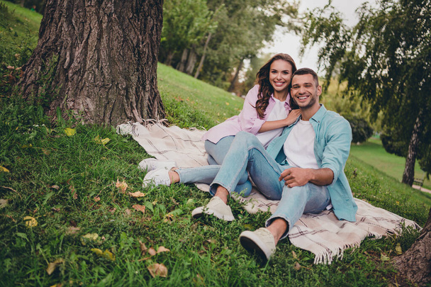Photo of funny charming young wife husband dressed pastel shirts sitting plaid blanket enjoying sunshine outdoors backyard. - Фото, зображення