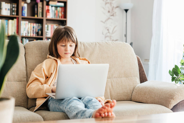 Koulutyttö opiskelee kotona kannettavan avulla. Lapsi katsoo webinaaria tai valmistautuu tenttiin verkossa. Etäopetus lapsille. - Valokuva, kuva