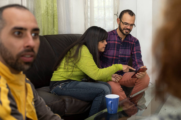 Lateinamerikanische Freunde plaudern, während sie zu Hause auf dem Sofa sitzen und sich amüsieren - Foto, Bild