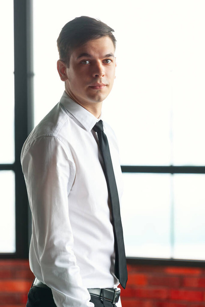 Portrait of young handsome businessman standing against window. - 写真・画像