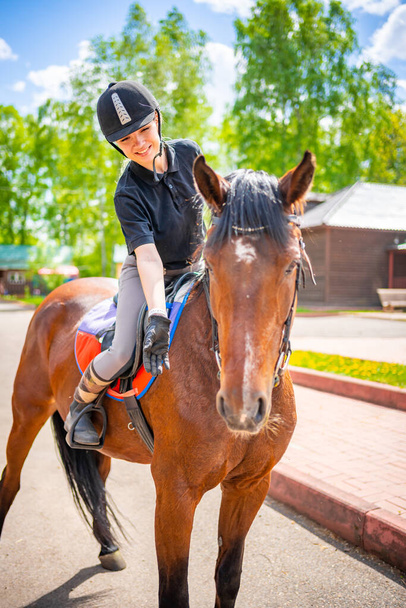 Милая молодая женщина в шлеме гладит свою коричневую лошадь. Высокое качество фото - Фото, изображение