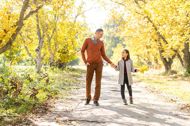 Очаровательная маленькая девочка с счастливым отцом, гуляющая в осеннем парке в солнечный день
. - Фото, изображение