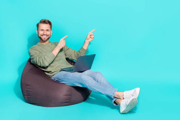 Full length photo of millennial blond guy hold laptop index promo wear sweater jeans sneakers isolated on turquoise background. - Foto, immagini