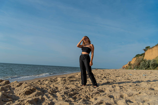 Woman wearing black dress walking on beach. See view - 写真・画像