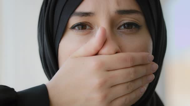 Female portrait indoors Islamic Arabian girl sad afraid Muslim woman Arab lady in black hijab looking at camera covers mouth with hands quiet silence discrimination stop talking oppression of women - Footage, Video