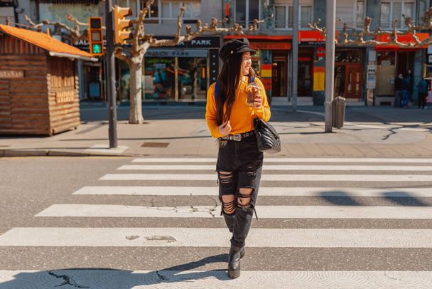joven asiático mujer cruzar un crosswalk mientras bebiendo un chocolate milkshake y turismo en un europeo ciudad. - Foto, imagen