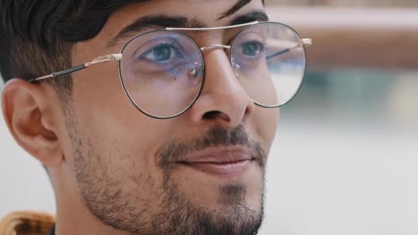 Αρσενικό πορτρέτο κοντινό πλάνο νεαρός γενειοφόρος ινδός τύπος με γυαλιά κοιτάζει μακριά χαρούμενος χαμογελαστός άντρας περιμένει για τη συνάντηση αξιολογεί nods κεφάλι σε έγκριση διαφημίζει οφθαλμικό κατάστημα μοντέλο μαθητή ποζάρουν σε εσωτερικούς χώρους - Πλάνα, βίντεο