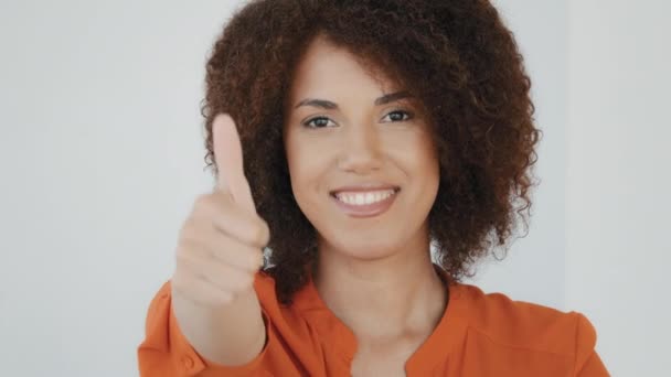 Портрет кудрявые волосы афроамериканка положительный двуличный модель девушка позирует в помещении, глядя на камеру, показывая жест одобрения поддержки согласиться рекомендация поднимает большой палец вверх хороший знак - Кадры, видео