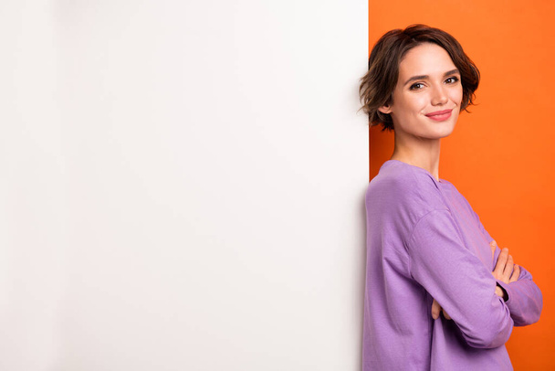 Photo of cute adorable lady wear violet sweatshirt arms crossed white poster empty space isolated orange color background. - 写真・画像