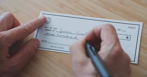 Hombre escribiendo un cheque para pagar por los servicios.Firmando un cheque en la mesa - Metraje, vídeo