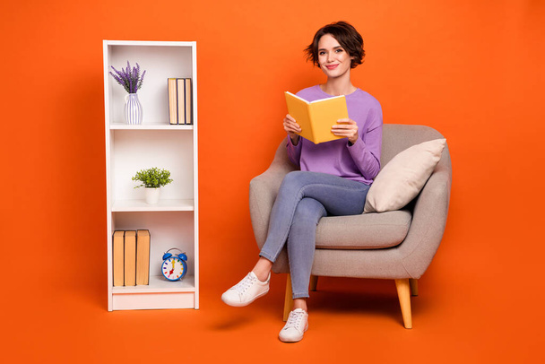 Full length photo of sweet cute lady wear violet sweatshirt sitting chair reading book isolated orange color background. - Φωτογραφία, εικόνα
