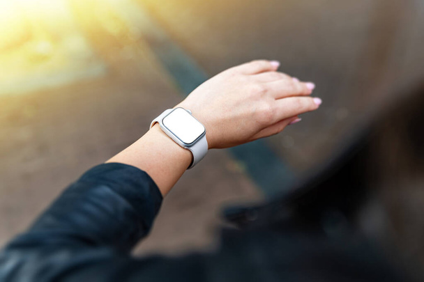 a woman checks something on a frameless smartwatch with a white blank screen - a template for mobile applications - Photo, Image