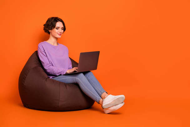 Full size portrait of pretty positive lady sitting cozy bag use wireless netbook isolated on orange color background. - Valokuva, kuva