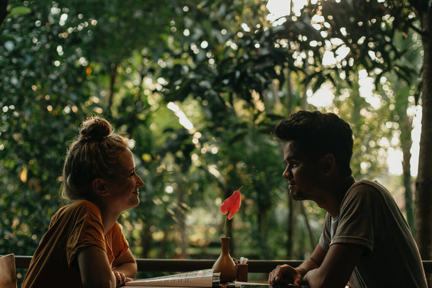 Young interracial couple looking at each other at a forest cafe table - Zdjęcie, obraz