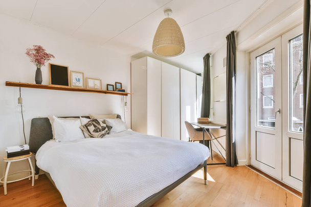 Home interior design of bedroom with bed and wooden wardrobe placed in corner near window in modern apartment - Foto, afbeelding