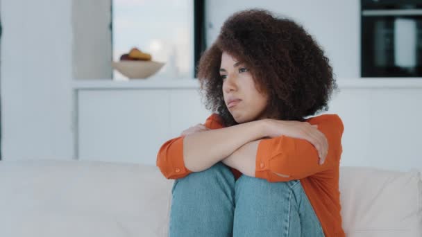 Одна одинокая напряженная афроамериканка сидит с грустной проблемой на домашнем диване, думая о проблемах, глядя в сторону плохого здоровья стресс расстроенный девушка чувствует себя нездоровым печаль неудачно решение - Кадры, видео