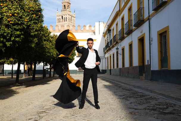 Ritratto di giovane e bello zingaro, vestito di scarpe nere e rosse che danza con un mantello di torero nero e giallo per le strade di seville. Flamenco patrimonio culturale dell'umanità. - Foto, immagini