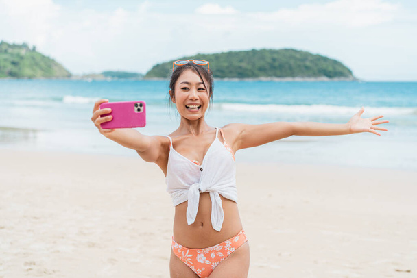 Portrait of happy smiling beautiful women taking a selfie photo on the beach. Pretty young Asian girl in casual looking clothes recording vlog video in bright sky - Foto, immagini