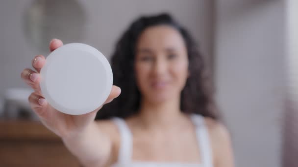 Out focus happy smiling young woman standing in bathroom holding cosmetic product in hand demonstrating jar of skin care cream advertise promotes facial skincare treatment hydration natural cosmetics - Footage, Video