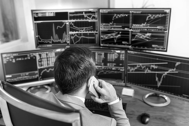 Over the shoulder view of computer screens ful of charts and data analyses and stock broker trading online. Black and white image. - 写真・画像