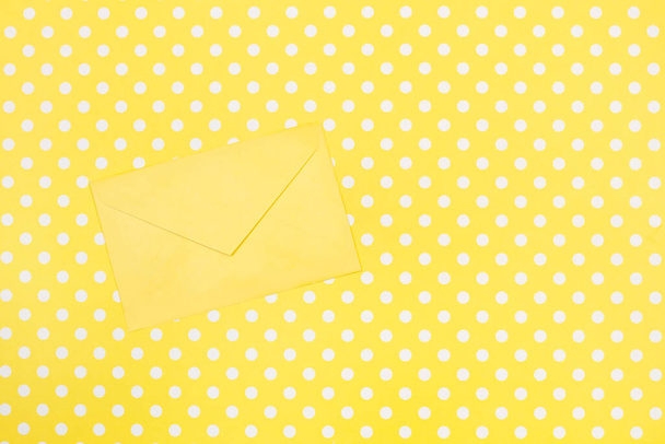 A yellow envelope on a yellow with white polka dots background with copy space - Fotó, kép