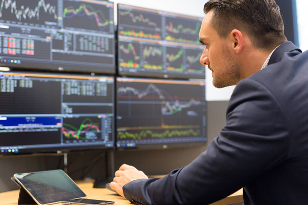 Stock broker trading online while accepting orders by phone. Traders office with multiple computer screens full of index charts and data analyses. - Photo, Image