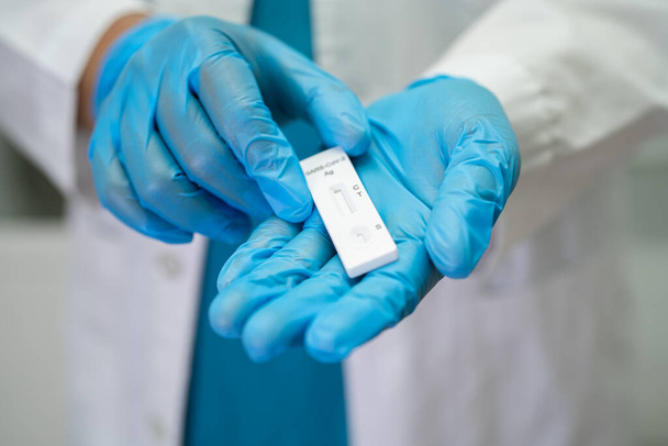 Un médecin asiatique en costume PPE montre un résultat positif au test avec le kit de test d'antigène de salive pour le coronavirus Covid-19 à l'hôpital. - Photo, image