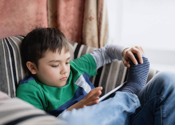 Portrét dítě hrát hru na tabletu sedí na pohovce, Mladý chlapec čtení nebo dělat domácí úkoly on-line na internetu doma, Dítě sledování karikatury on-line na digitální podložce.Home vzdělávání, Zpět do školy koncept - Fotografie, Obrázek