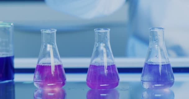 Ein medizinisches Forschungsexperiment in einem Chemielabor mit farbverändernder Flüssigkeit. Nahaufnahme einer Spritze, die blaue alkalische oder saure Chemikalien in eine Reihe von Erlenmeyerkolben gießt, um eine stabile Lösung zu schaffen. - Filmmaterial, Video