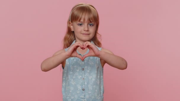 I love you. Smiling young preteen child girl kid makes heart gesture demonstrates love sign expresses good feelings and sympathy. Little toddler children isolated alone on studio pink background - Materiał filmowy, wideo