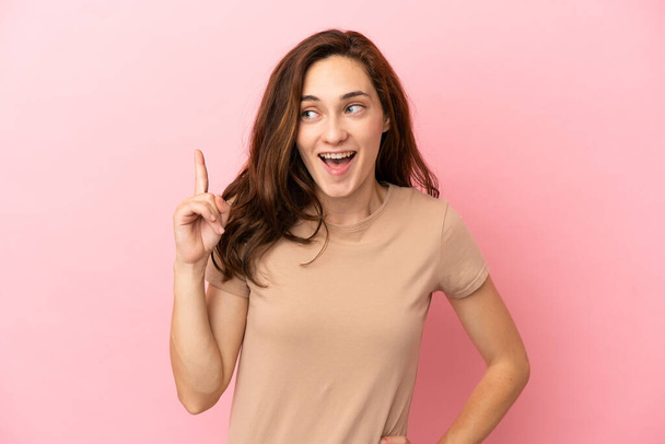 Молода біла жінка ізольована на рожевому фоні думаючи, що ідея спрямовує палець вгору
 - Фото, зображення
