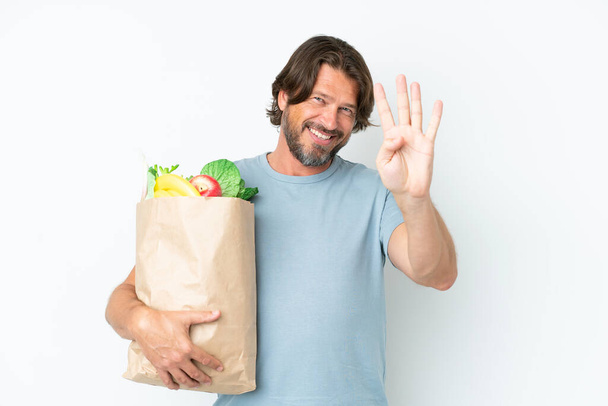 Senior dutch man holding grocery shopping bag over isolated background happy and counting four with fingers - Foto, afbeelding