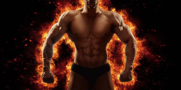 Brutal strong athletic Bodybuilder posing. Fire and spark explosion in the background. Bodybuilding and healty life concept. - 写真・画像